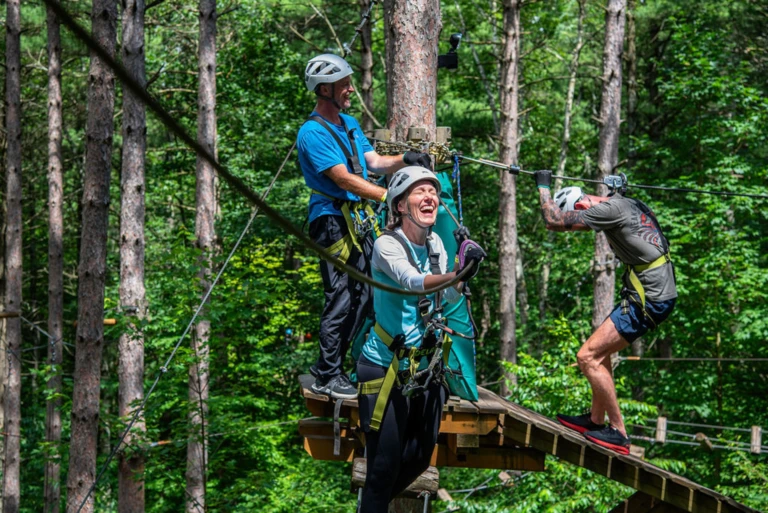 Guests laughing while navigating aerial obstacles at Treetop Trekking Ganaraska, surrounded by towering red pine forest in Ontario