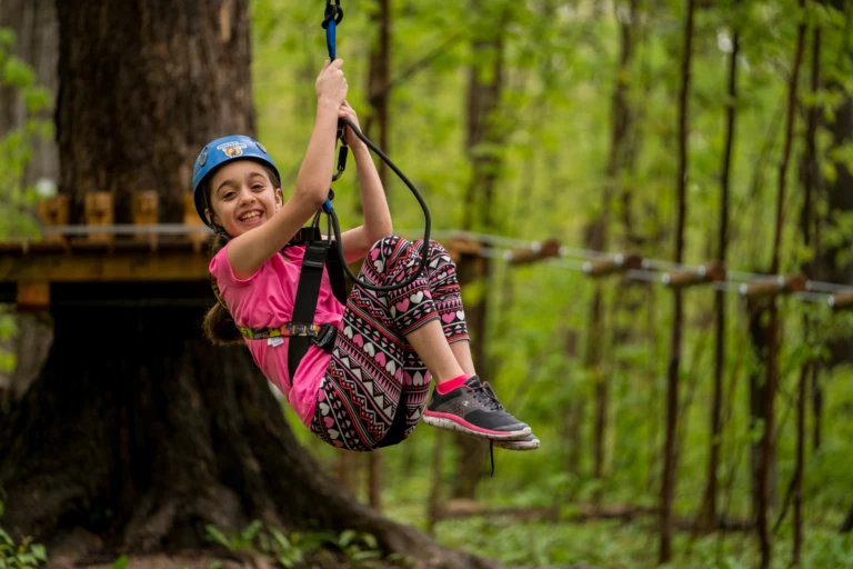 A smiling girl in a helmet gliding on a zipline through the forest at Treetop Trekking Stouffville